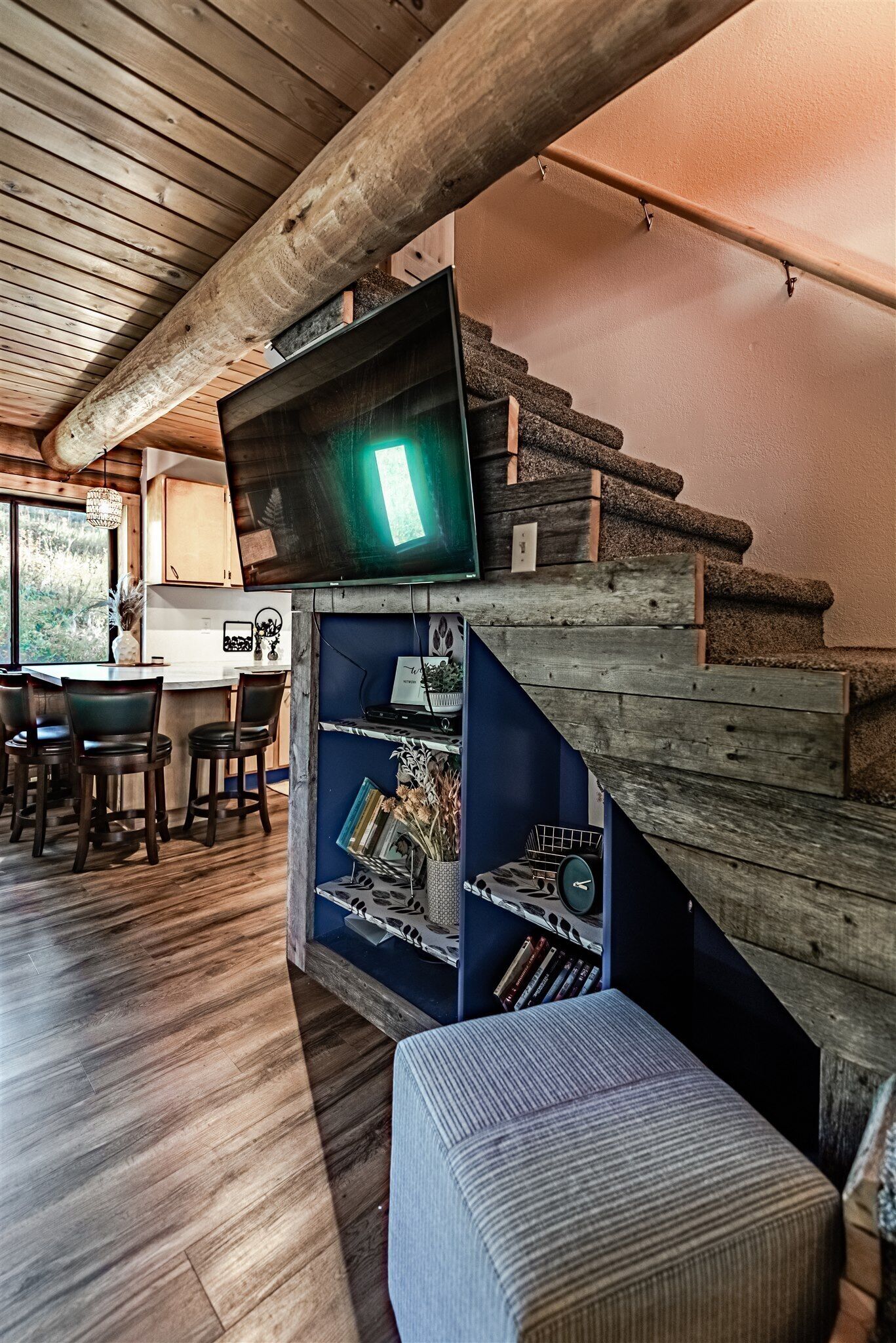 Una escalera de madera conduce a una zona de cocina con un televisor de pantalla plana montado en la pared.
