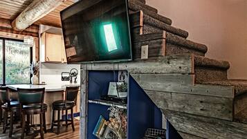 Una escalera de madera conduce a una zona de cocina con un televisor de pantalla plana montado en la pared.