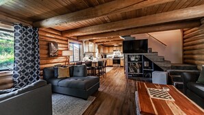 Interior de uma cabana de toras com sala de estar, sala de jantar, cozinha e escada.