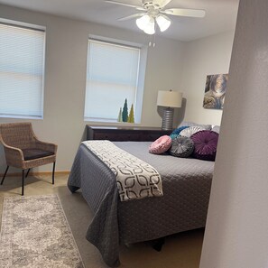 Un dormitorio con cama, una silla, una lámpara y una ventana con persianas.