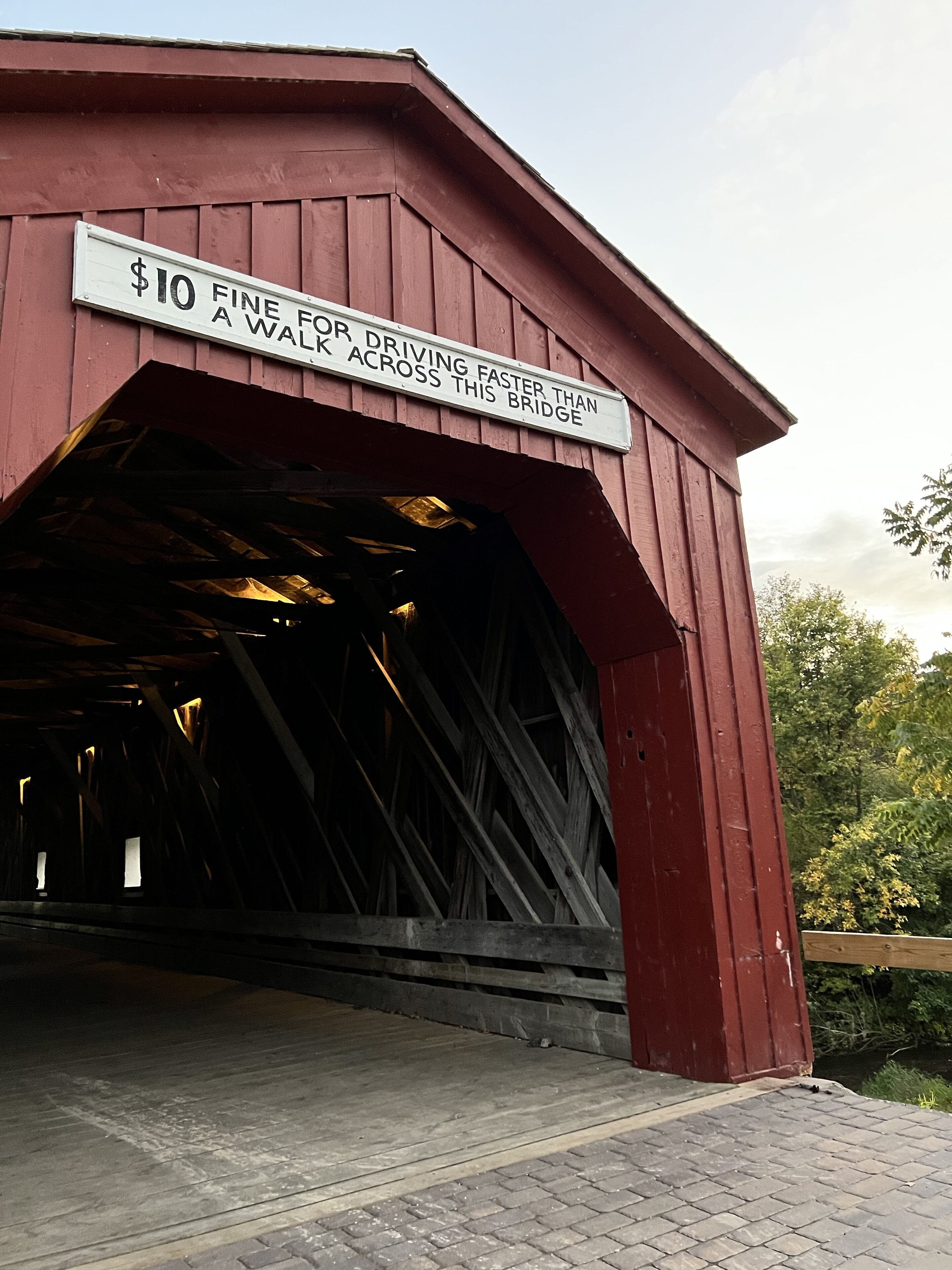 A red covered bridge with a sign indicating a $10 fine for driving faster than the bridge's speed limit.
