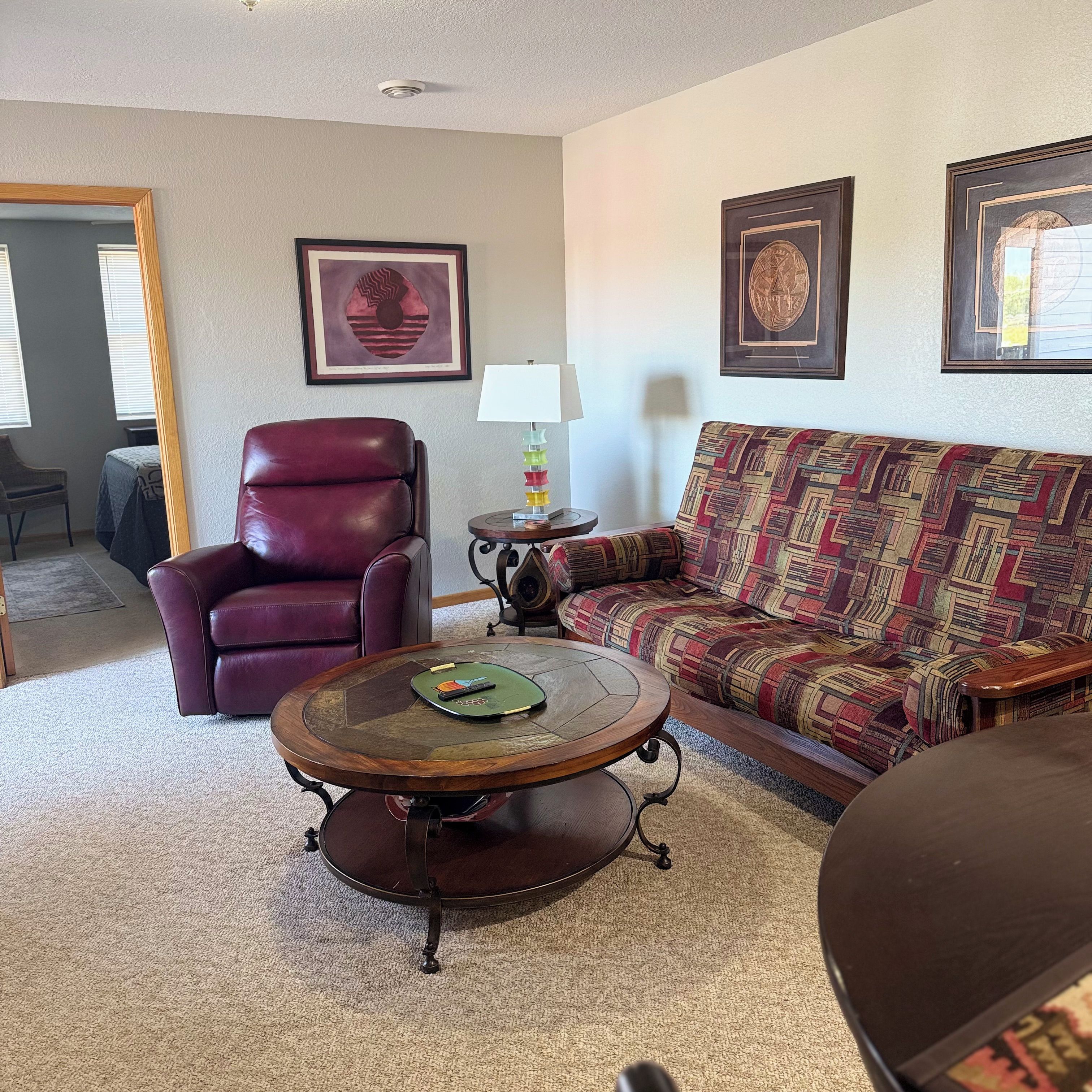 A living room with a leather chair, a patterned sofa, a coffee table, and framed artwork on the walls.
