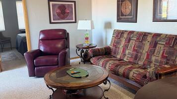 A living room with a leather chair, a patterned sofa, a coffee table, and framed artwork on the walls.
