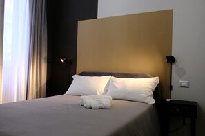 A neatly made bed with white linens and a folded towel, a bedside lamp, and a wall switch on a nightstand. - MATTEOTTI ROOMS (Matera)