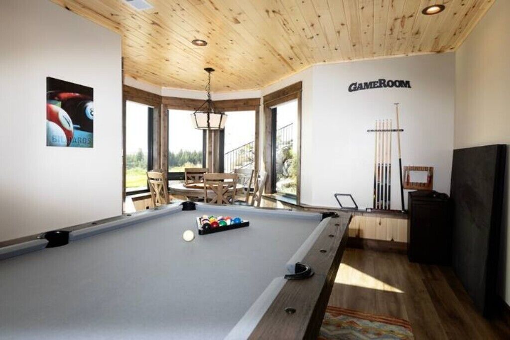 Une table de billard avec des billes, un porte-queue et une enseigne « SALLE DE JEUX » dans une pièce dotée de plafonds en bois et de grandes fenêtres.