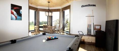 Une table de billard avec des billes, un porte-queue et une enseigne « SALLE DE JEUX » dans une pièce dotée de plafonds en bois et de grandes fenêtres.