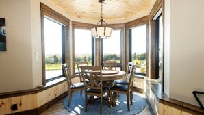 Un comedor con una mesa redonda y sillas, ventanas amplias y techo de madera.