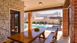 Un patio con mesa y bancos de madera, una piscina y zona de estar al aire libre.