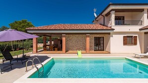 Una piscina con tobogán, sillas de descanso y una zona de patio con una sombrilla morada.