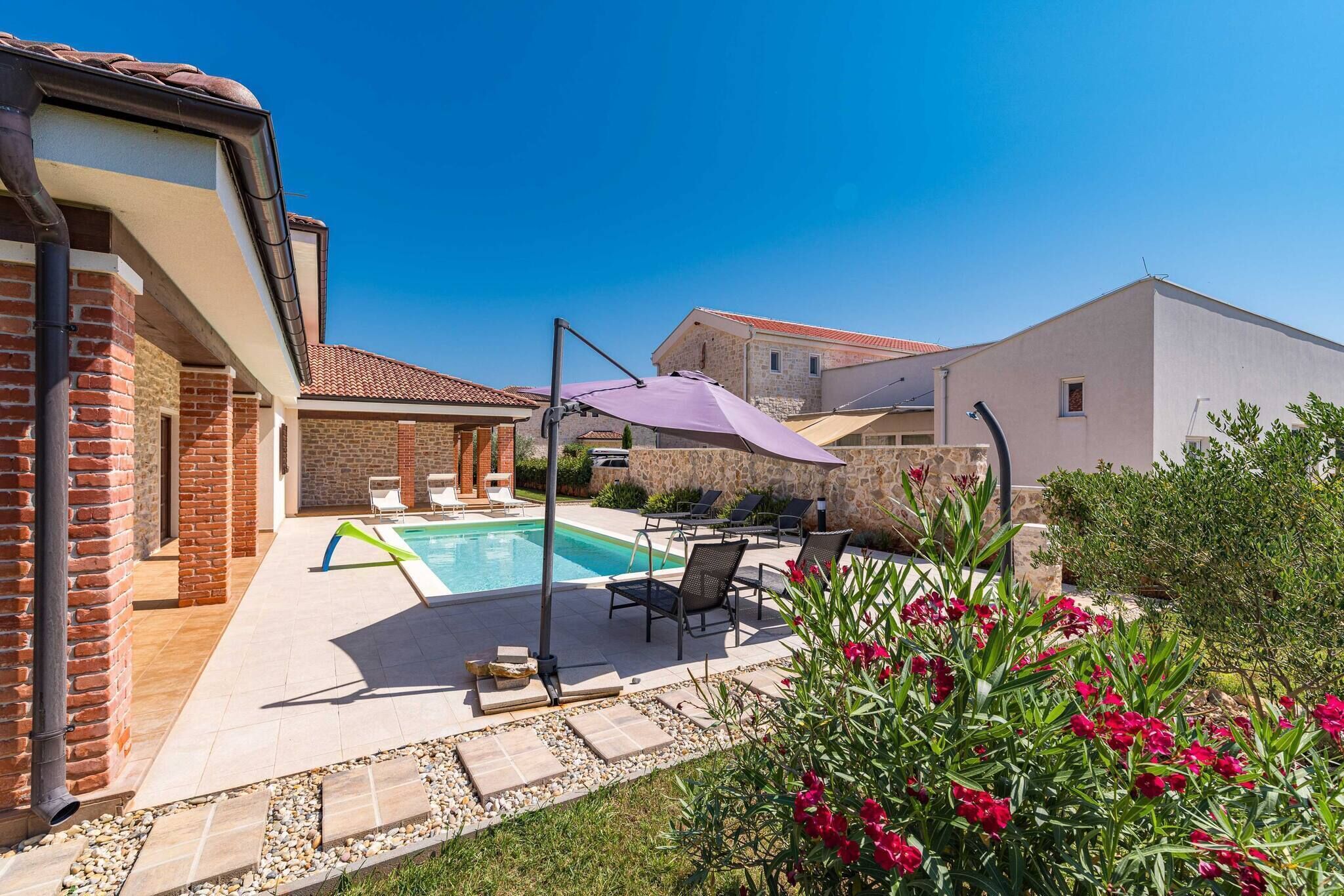 A swimming pool with lounge chairs and a pergola, surrounded by a garden with red flowers.
