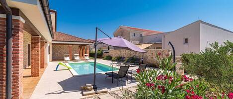 A swimming pool with lounge chairs and a pergola, surrounded by a garden with red flowers.