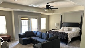 A bedroom with a large bed, a dark-colored sectional sofa, a small table, and a ceiling fan. - Premier Location! Lake View! (Arnolds Park)