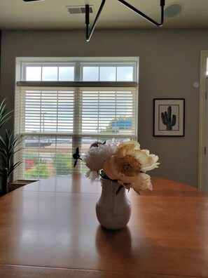 A room with a large window, a cactus artwork on the wall, and a vase with flowers on a table.