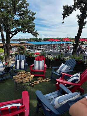 Outdoor seating with Adirondack chairs, a fire pit, and a view of a waterfront restaurant.