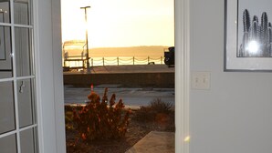 A room with a view of the beach and ocean at sunset, a black leather bench, and a framed picture on the wall. - Premier Location! Lake View! (Arnolds Park)