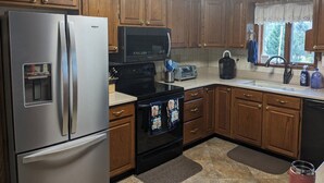 Una cocina con armarios de madera, un refrigerador de acero inoxidable, un microondas, un tostador y una cafetera.