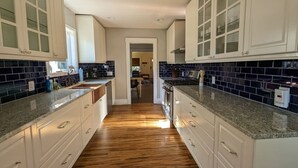 A kitchen with white cabinets, dark blue backsplash, and wooden flooring. - 2BR Craftsmen Greenlake Home + Backyard + Firepit (Seattle)