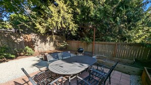 A patio with a round table and chairs, surrounded by a wooden fence and trees. - 2BR Craftsmen Greenlake Home + Backyard + Firepit (Seattle)