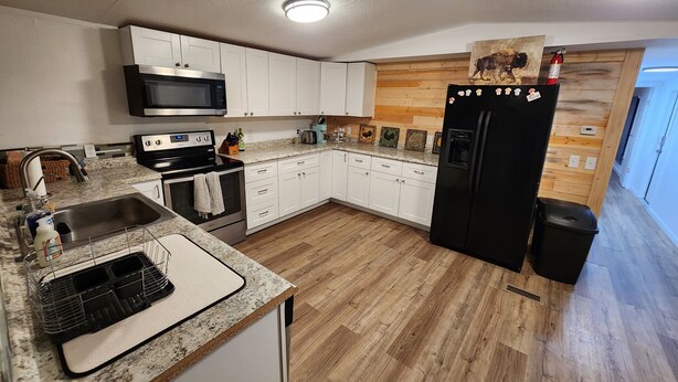 A modern kitchen with white cabinets, a black refrigerator, stainless steel appliances, and a wooden floor. - Country Living located Mid-Way between Granbury and Glen Rose.  (Granbury)