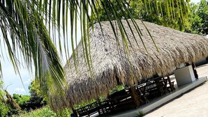 A thatched-roof structure with a concrete base, surrounded by sand and greenery, including palm trees and other tropical plants. - HOTEL LAS CASITAS DE MAR ADENTRO  (Rosario Islands)