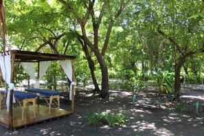 A wooden deck with blue cushions and a canopy, surrounded by trees in a park setting. - HOTEL LAS CASITAS DE MAR ADENTRO  (Rosario Islands)