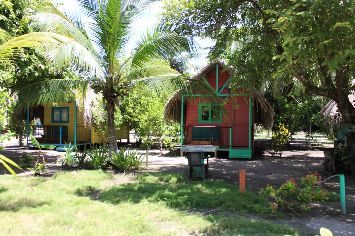 A tropical setting with thatched-roof huts surrounded by lush greenery and palm trees.