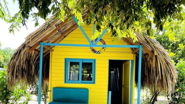 A small, single-story structure with a thatched roof and a bright yellow exterior. It features a blue-framed window and a wooden bench outside. - HOTEL LAS CASITAS DE MAR ADENTRO  (Rosario Islands)