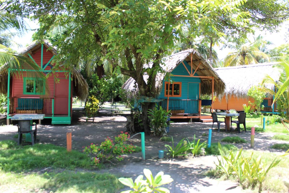 A tropical resort with thatched-roof cottages, outdoor seating, and lush greenery.