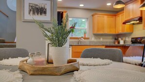 A dining table with a white placemat, a wooden tray with salt and pepper shakers, and a textured white vase with green foliage. - Baker Bliss | Hot Tub · Fire Pit · Pet-Friendly · Mt. Baker Gateway (Deming)
