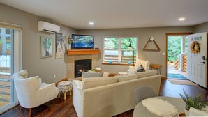 A living room with a fireplace, a television, and a door leading outside. - Baker Bliss | Hot Tub · Fire Pit · Pet-Friendly · Mt. Baker Gateway (Deming)