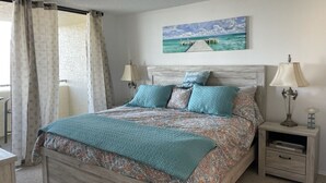 Un dormitorio con una cama, dos mesitas de noche, una lámpara de noche, una ventana con cortinas y un cuadro colgado en la pared.