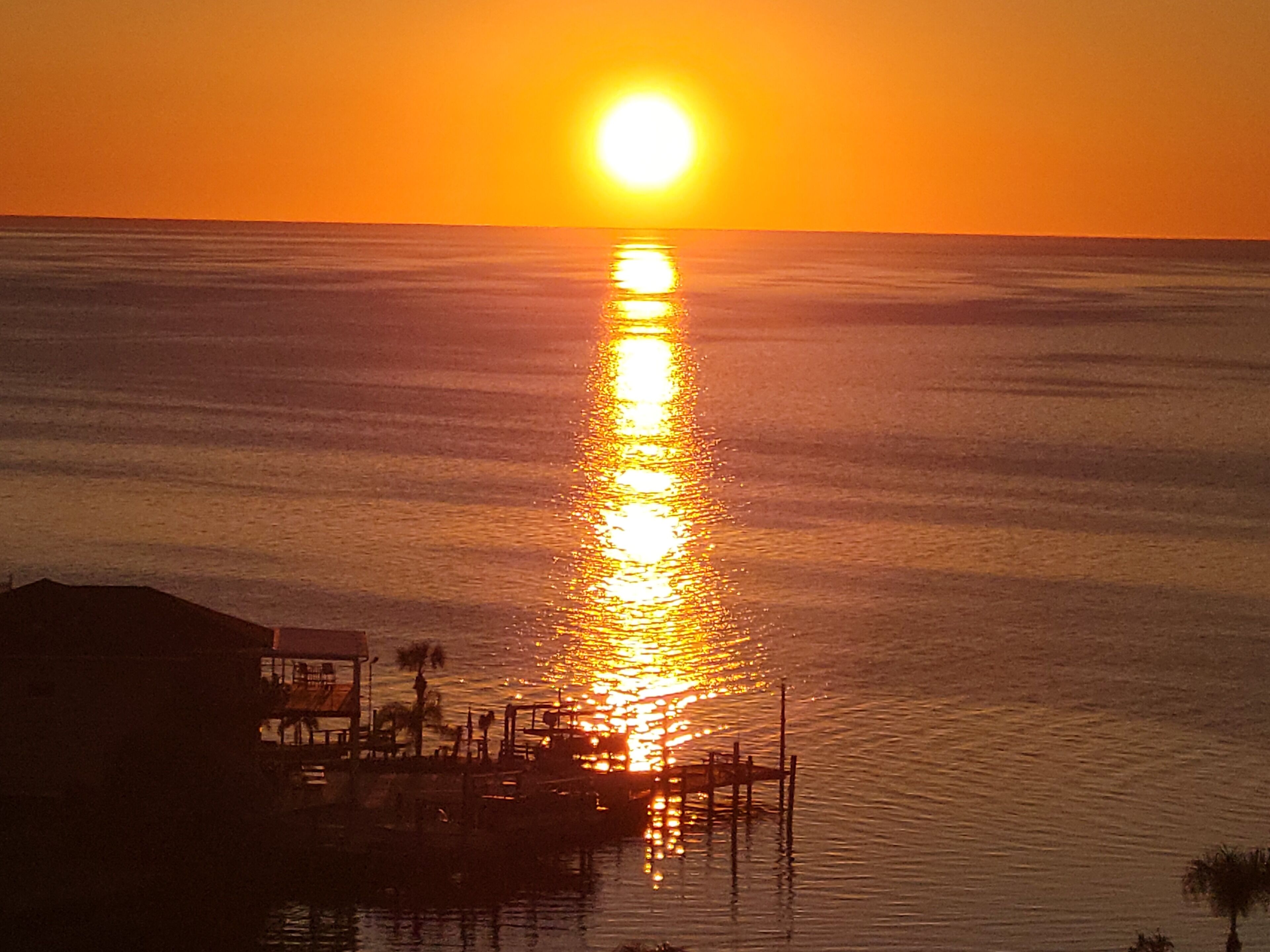 A sunset over a calm sea with a pier extending into the water.