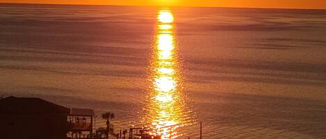 A sunset over a calm sea with a pier extending into the water.