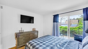 Un dormitorio con cama, cómoda, televisor y vistas a zonas verdes.