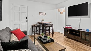 Una sala de estar con un sofá gris, una mesita de centro con una bandeja, un televisor y un mueble de entretenimiento de madera.