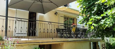 A covered outdoor seating area with a table and chairs, a large umbrella, and a railing.