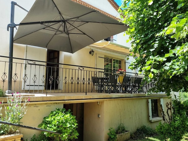 Uma área de estar coberta ao ar livre, com mesa, cadeiras, um grande guarda-sol e um corrimão.