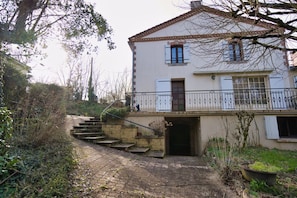 Uma casa de dois andares com telhado de telhas, porta de entrada e pequena escadaria que leva até ela.