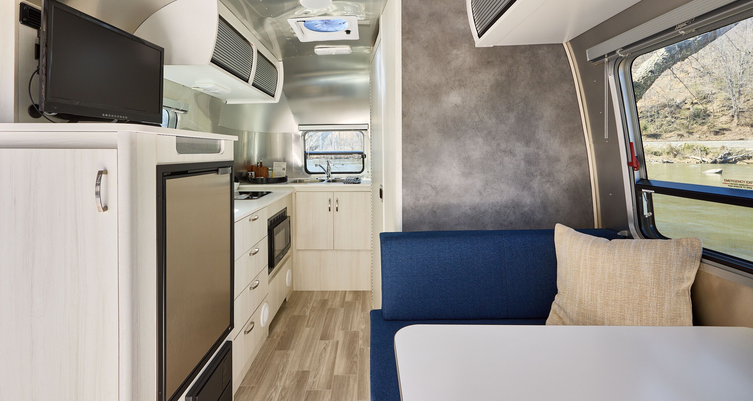 Un intérieur de camping-car compact comprenant un coin cuisine, un canapé bleu et une fenêtre donnant sur un paysage naturel.