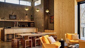 Eine moderne Küche mit Holzschnitzereien, ein Essbereich mit großem Tisch und Bänken sowie eine Sitzecke mit gelben Sofas.