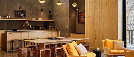 Una cocina moderna con armarios de madera, un comedor con una mesa grande y bancos, y una zona de estar con sofás amarillos.