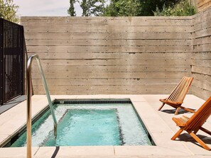 A rectangular pool with a metal ladder, two wooden lounge chairs, and a concrete wall. - AutoCamp Asheville (Asheville)