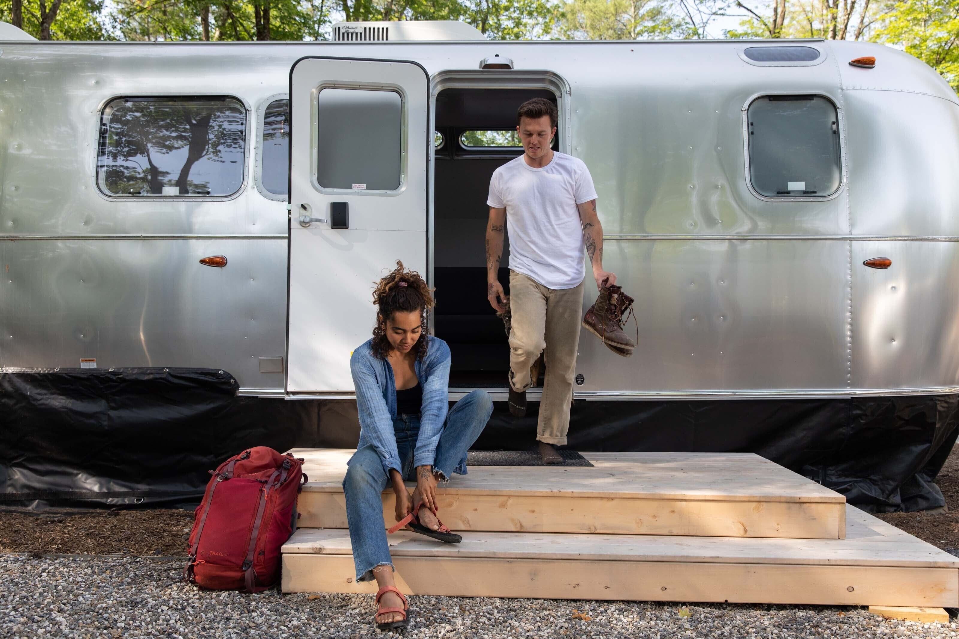 A silver trailer with a door open, steps leading up to it, and a red bag on the ground.