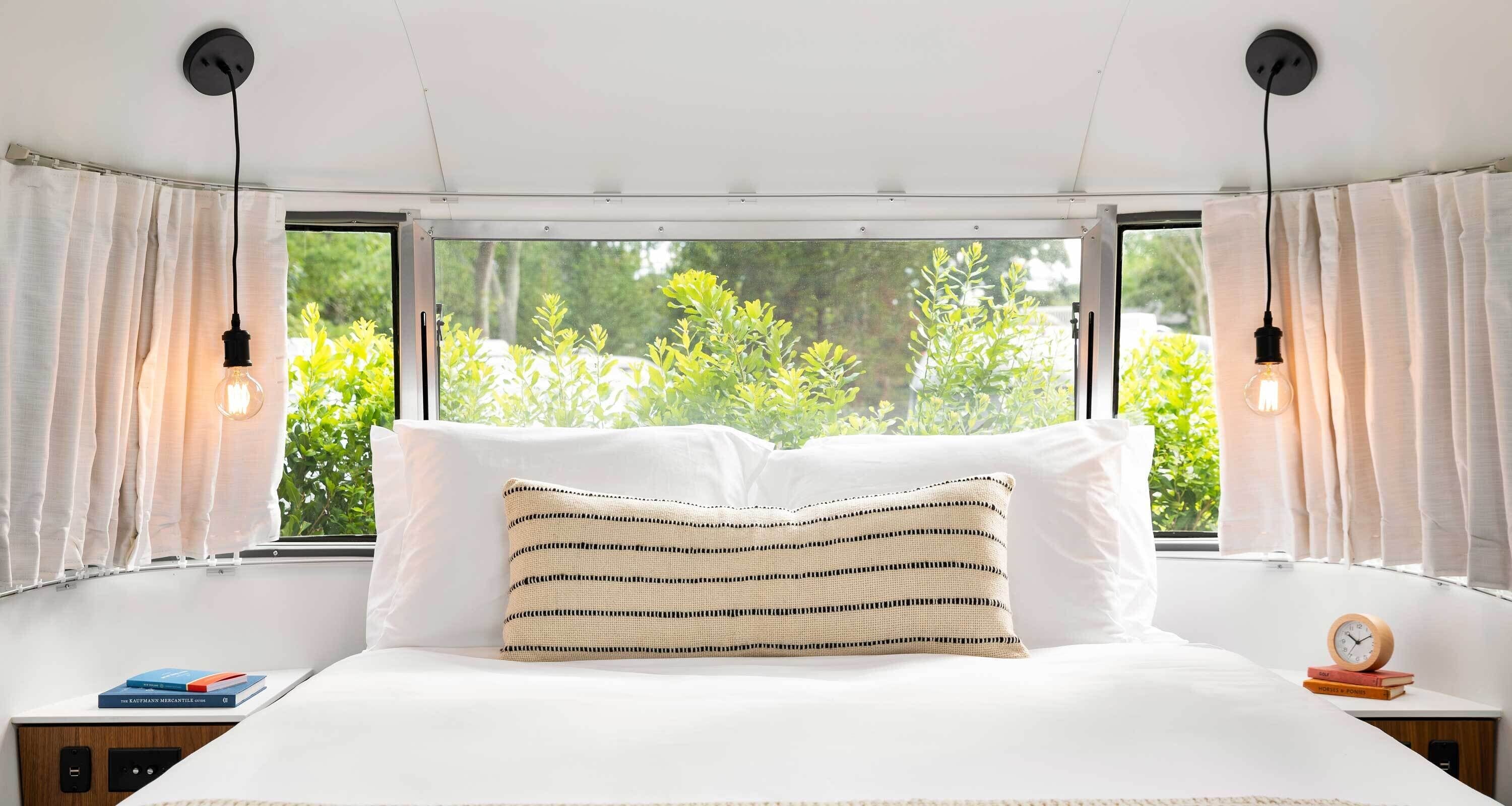A bedroom with a large bed, two bedside tables, a window with curtains, and a view of greenery outside.
