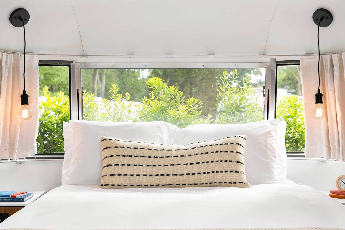 Un dormitorio con una cama grande, dos mesitas de noche, una ventana con cortinas y vistas al exterior.