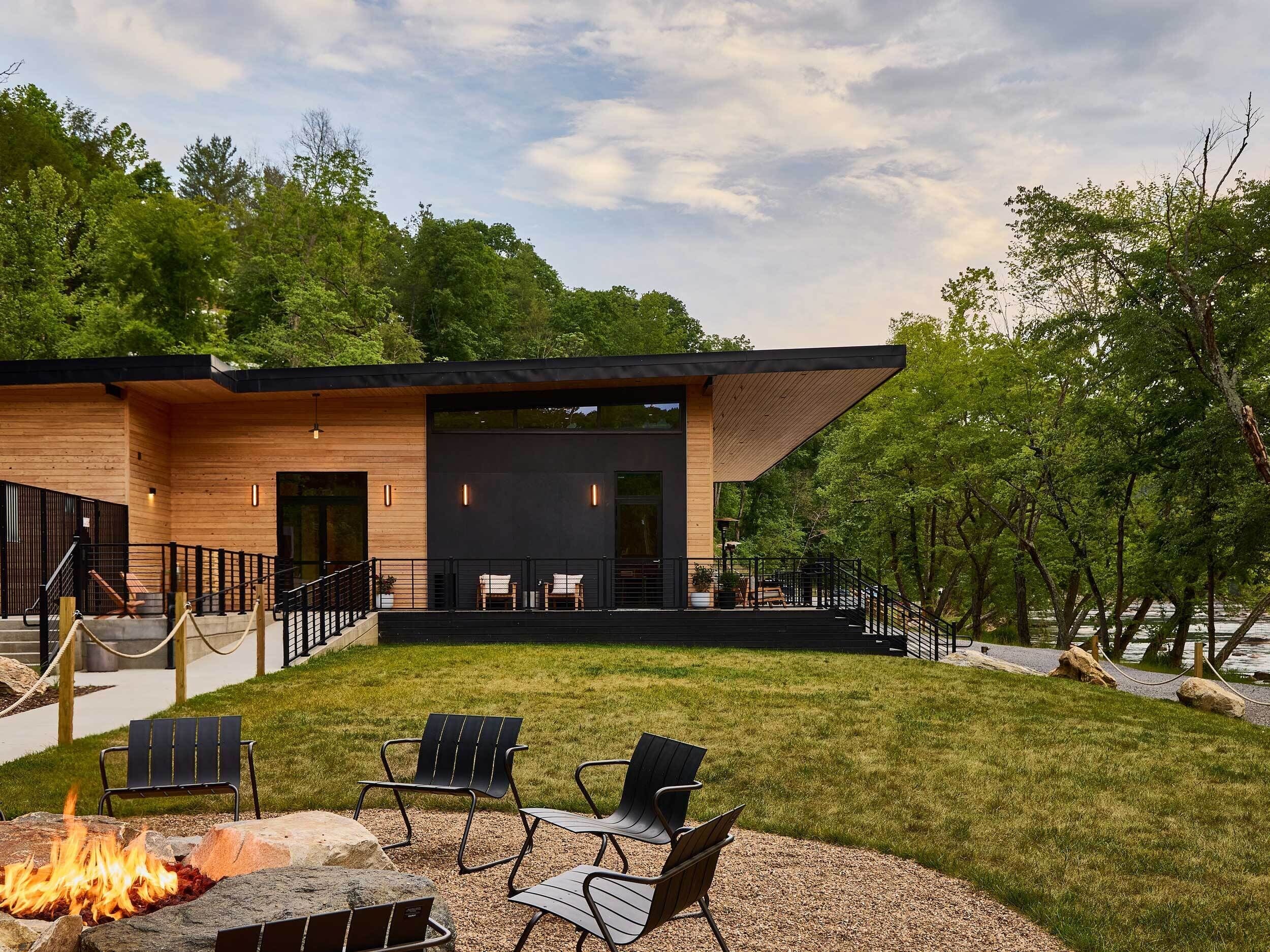 A modern building with a covered outdoor seating area, a fire pit, and a view of a lake.