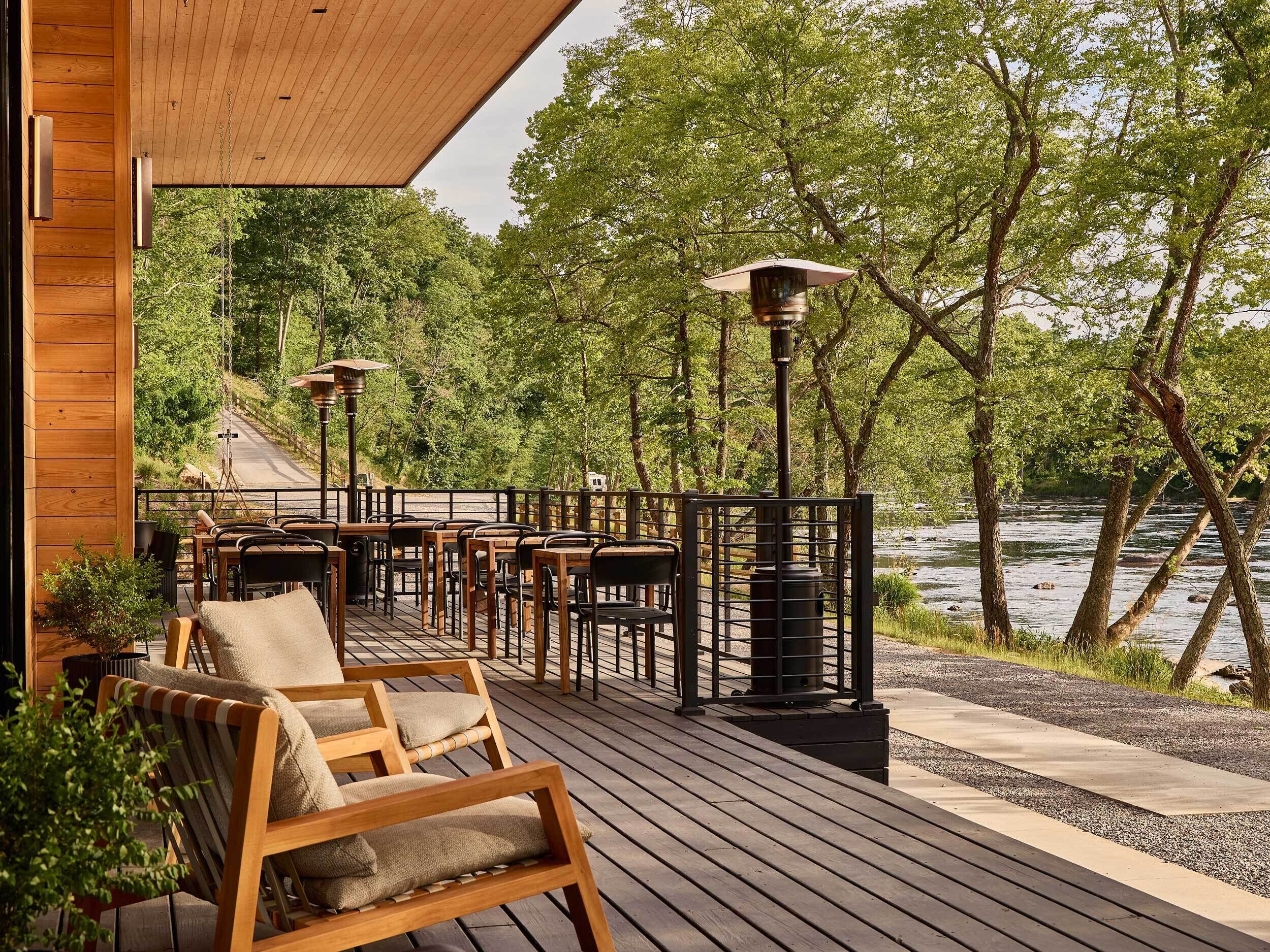 A wooden deck with outdoor seating, a view of a river, and a forested area.