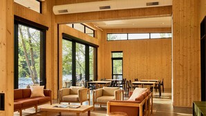 Ein geräumiges Zimmer mit großen Fenstern, Holzwänden und einer Mischung aus Sitzgelegenheiten, darunter Sofas und Sessel.