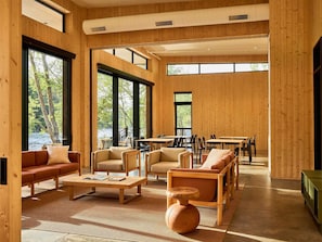 A spacious room with large windows, wooden walls, and a mix of seating arrangements including sofas and chairs.