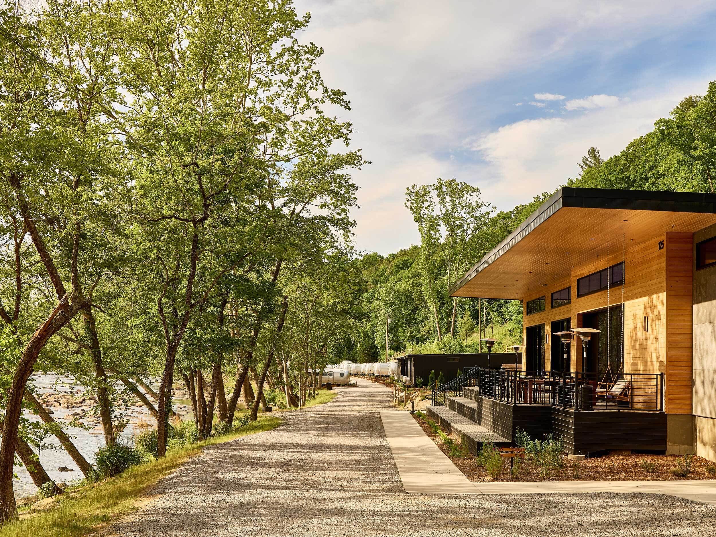 A modern building with a wooden facade, a gravel driveway, and a river on one side.